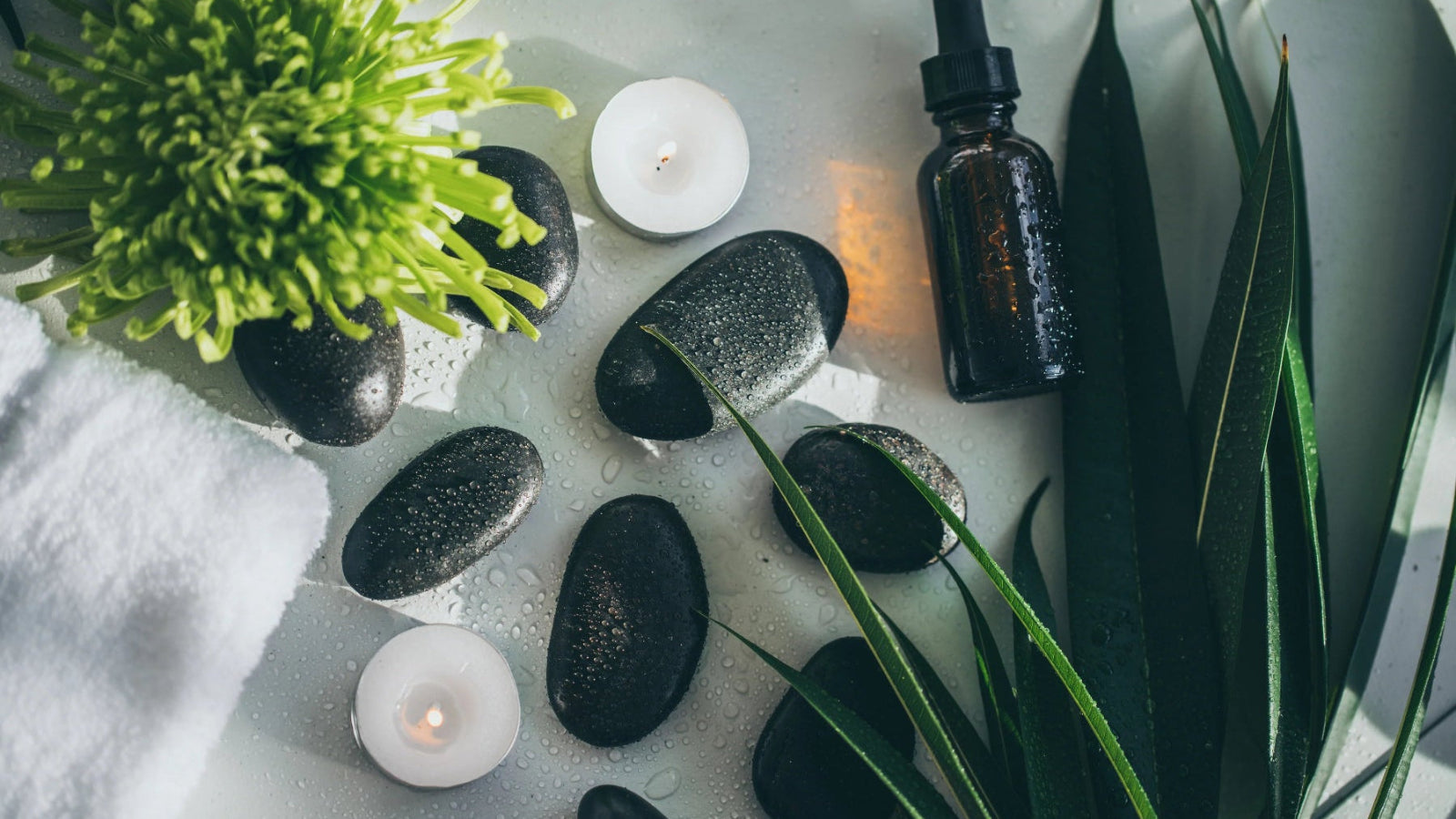 Aromatherapy setup with essential oil dropper, candles, and stones on a white surface.