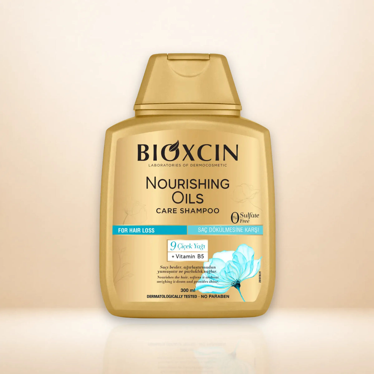 A bottle of BIOXCIN Nourishing Oils Care Shampoo in a metallic gold color, featuring a matching gold cap, set against a soft beige gradient background with a subtle reflection at the bottom.