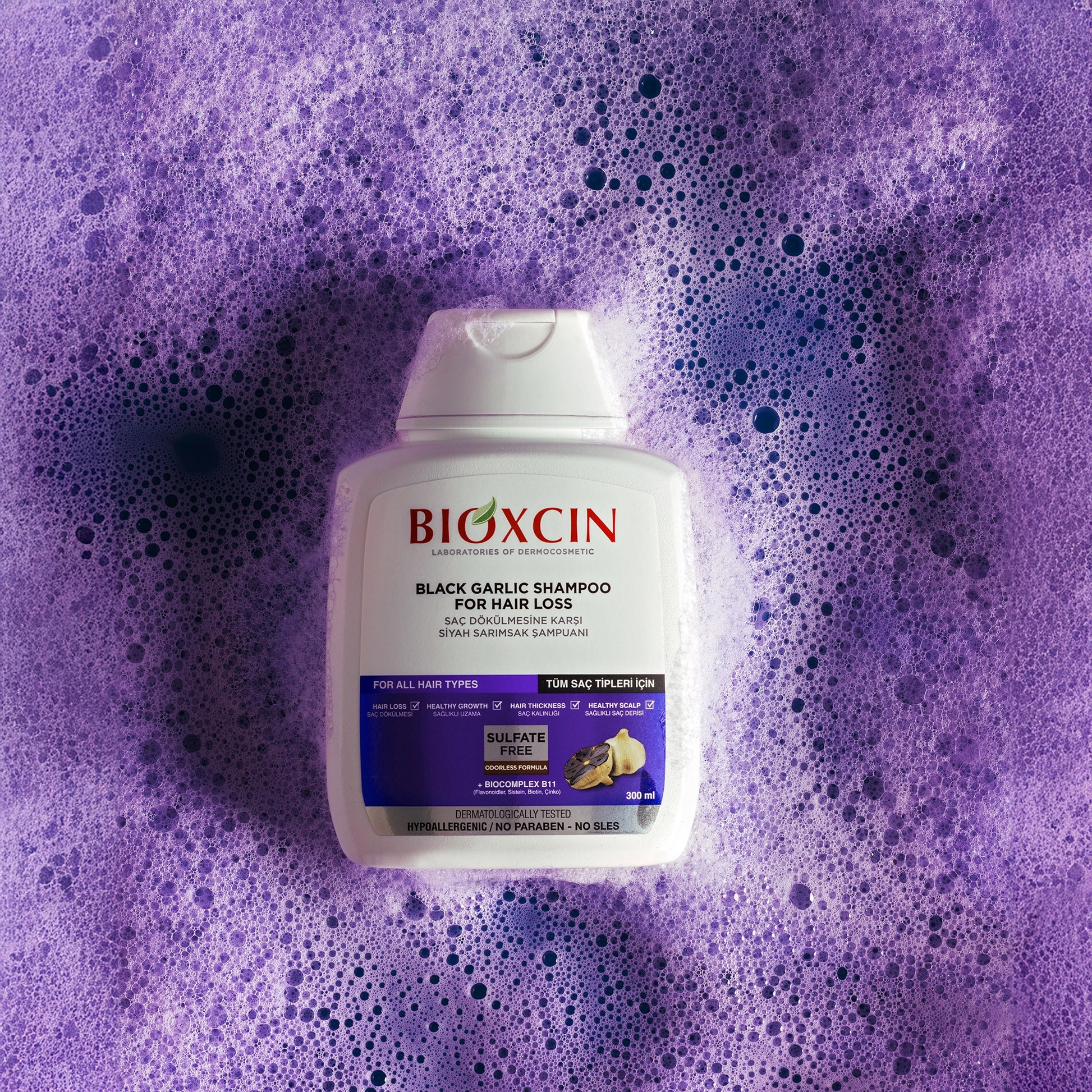Bioxcin black garlic shampoo bottle on a purple background with soap bubbles