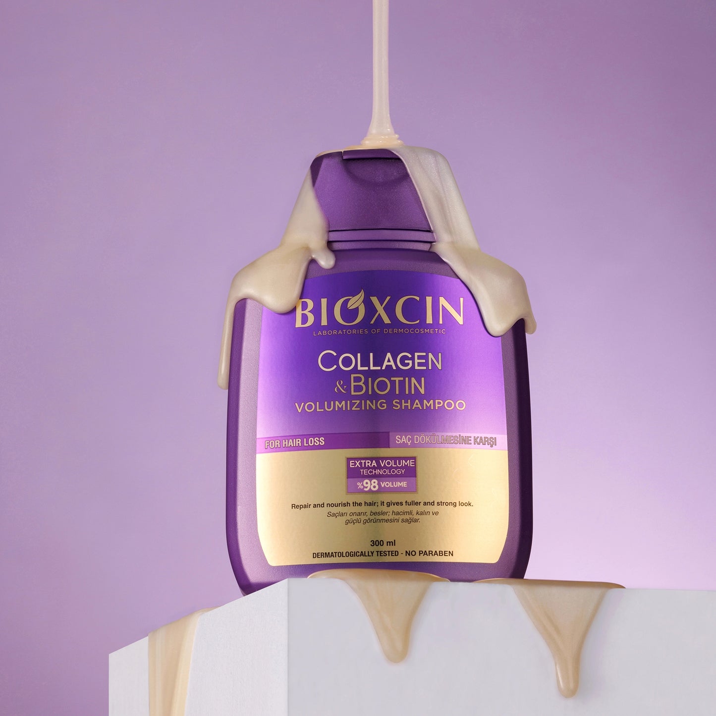 Bioxcin Collagen & Biotin shampoo bottle with purple label on a white stand against a purple background