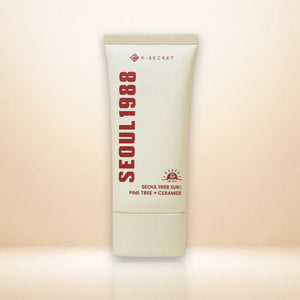 A single cream-colored cosmetic tube for K-SECRET Seoul 1988 Sun, standing upright against a warm beige gradient background.
