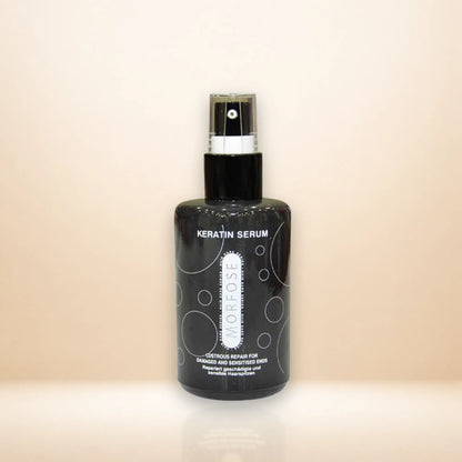 A black spray bottle of Morfose Keratin Serum with a silver and black pump, standing on a reflective beige surface against a solid beige background.