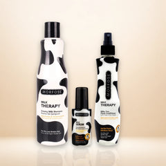 Three Morfose Milk Therapy hair care products with a black and white cow print design, including a shampoo bottle, a serum bottle, and a conditioner spray bottle, arranged on a reflective beige surface.