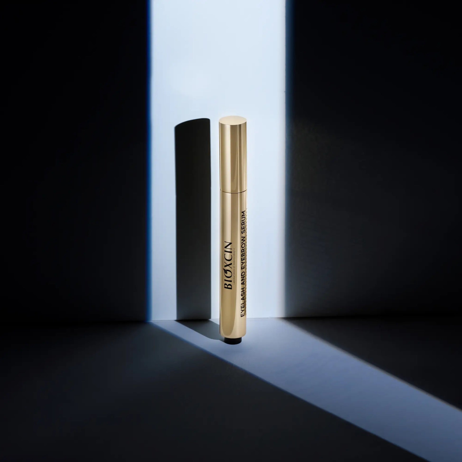 Gold Bioxcin eye brow and lash serum tube on a black and white background