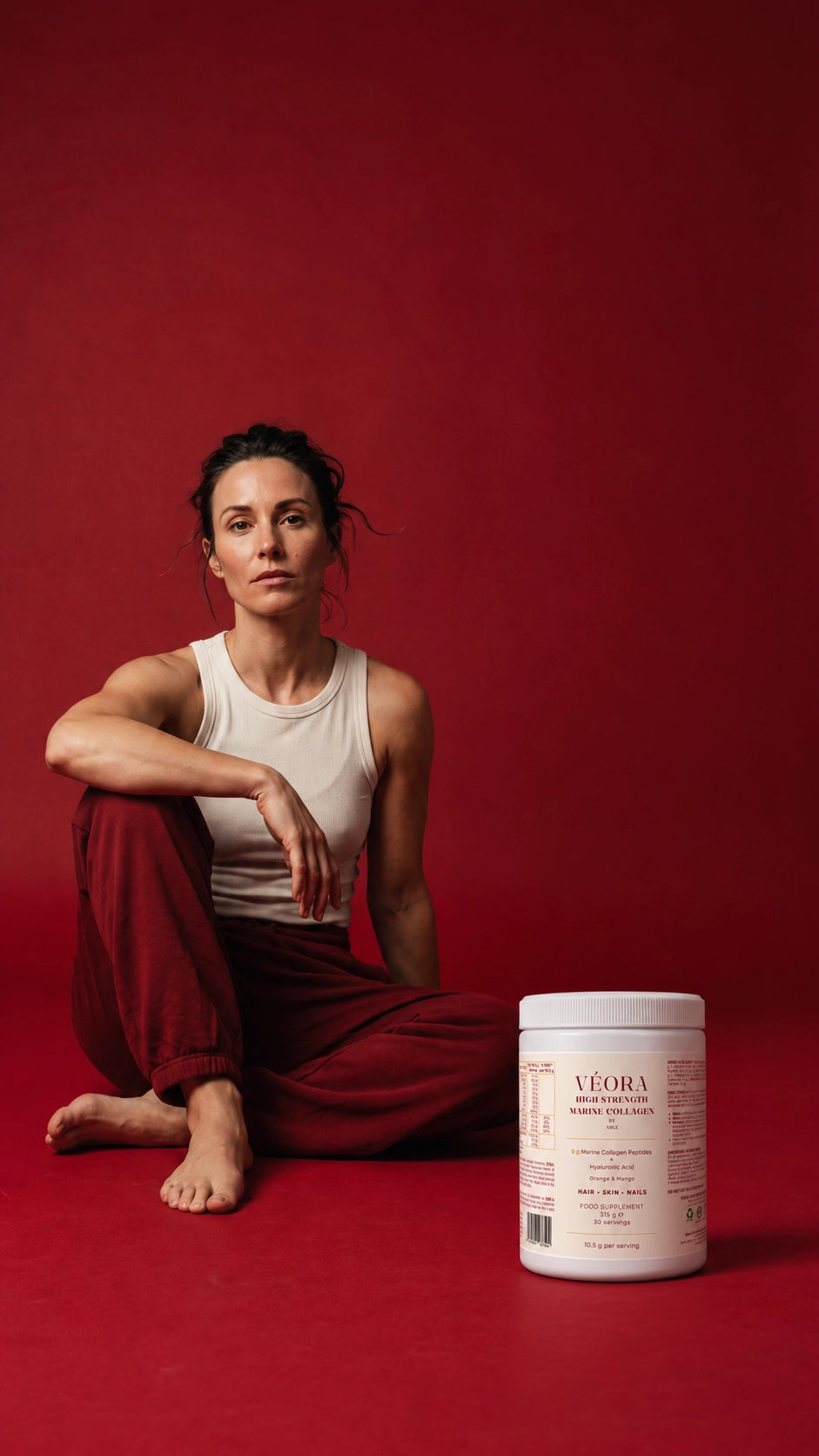 VÉORA Orange and Mango marine collagen powder tub in a burgundy studio setting