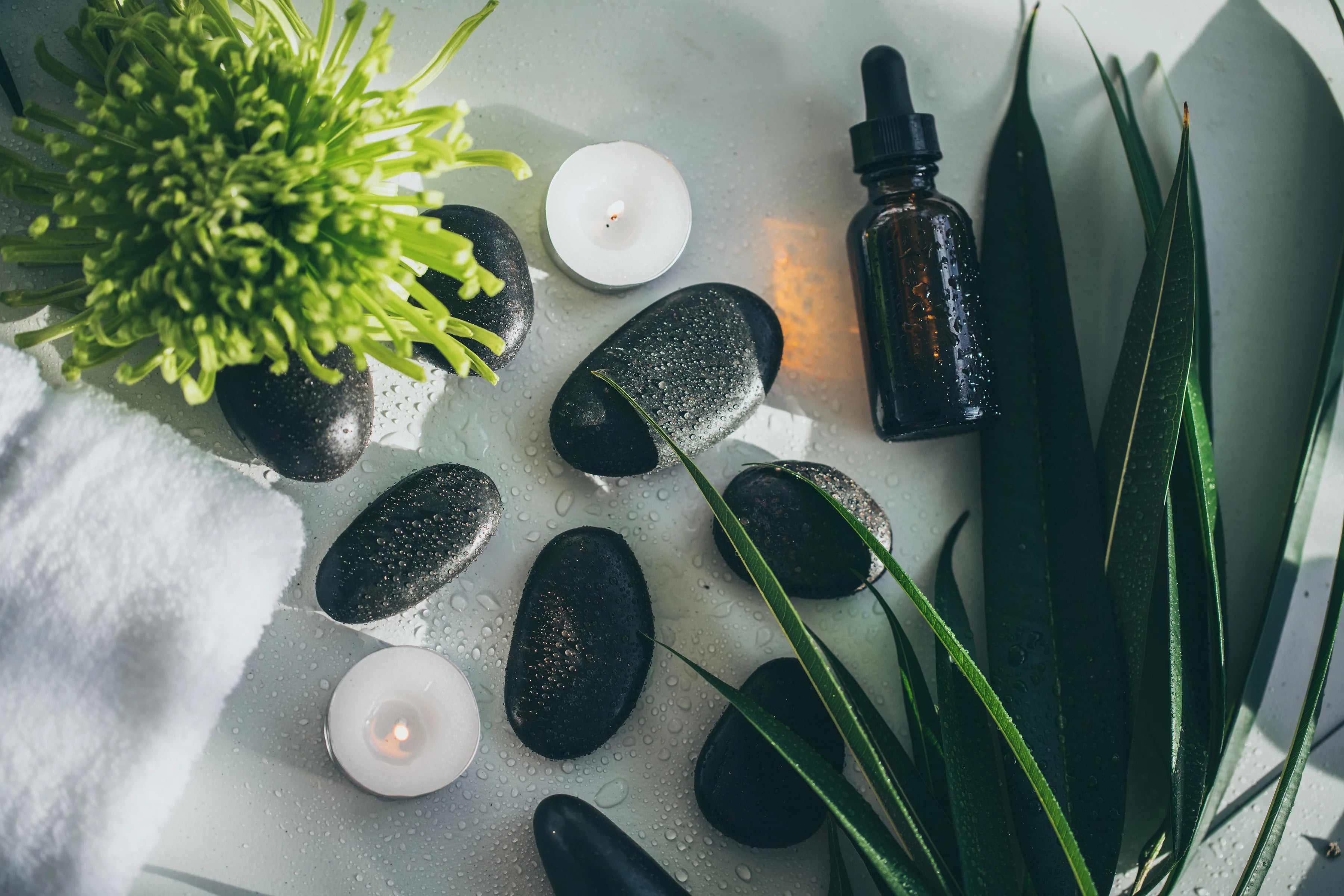 Aromatherapy setup with essential oil dropper, candles, and stones on a white surface.